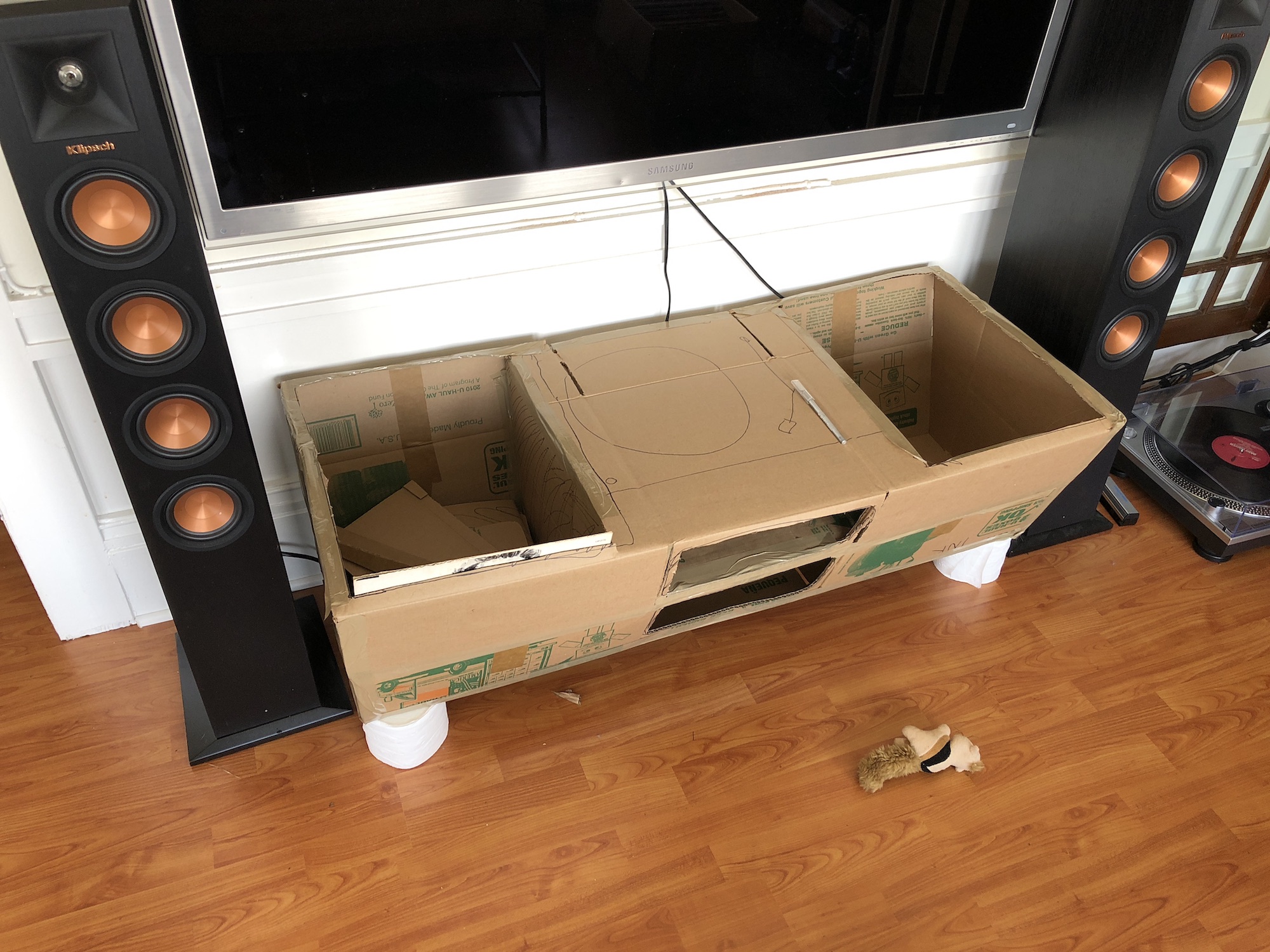 A very rough looking media center, made of cardboard, with two side storage areas for records and a record player scrawled on the surface with a sharpie